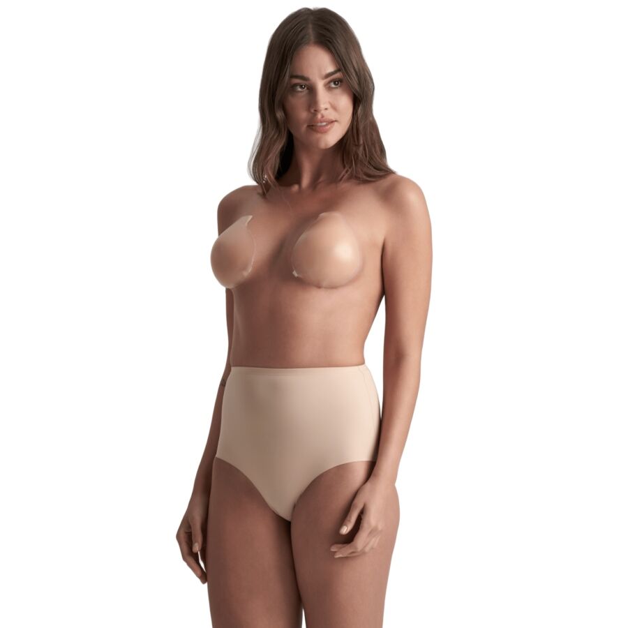 Femme debout portant les bonnets adhésifs silicone Bye Bra avec une culotte gainante beige